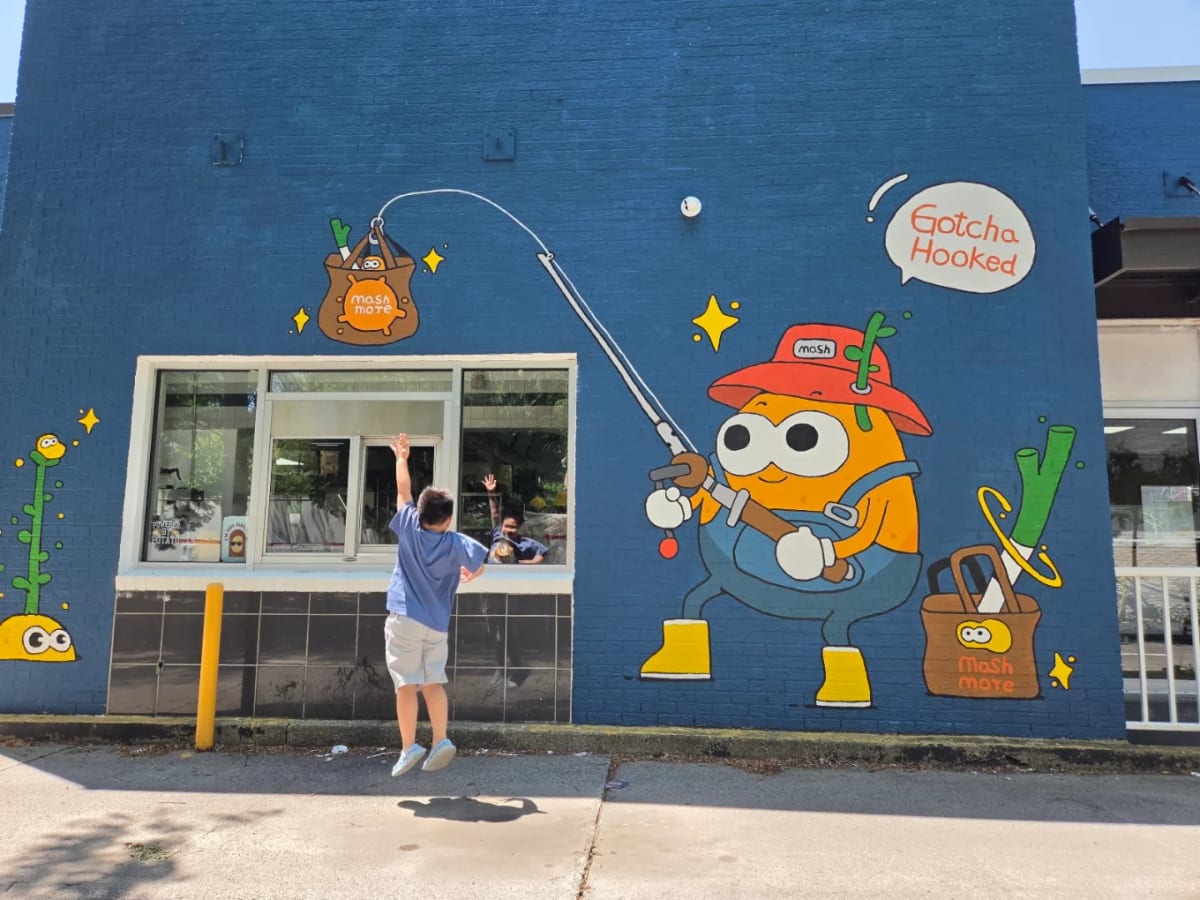 A child reaching up at the MashMore drive-thru window beside the Gotcha Hooked mural